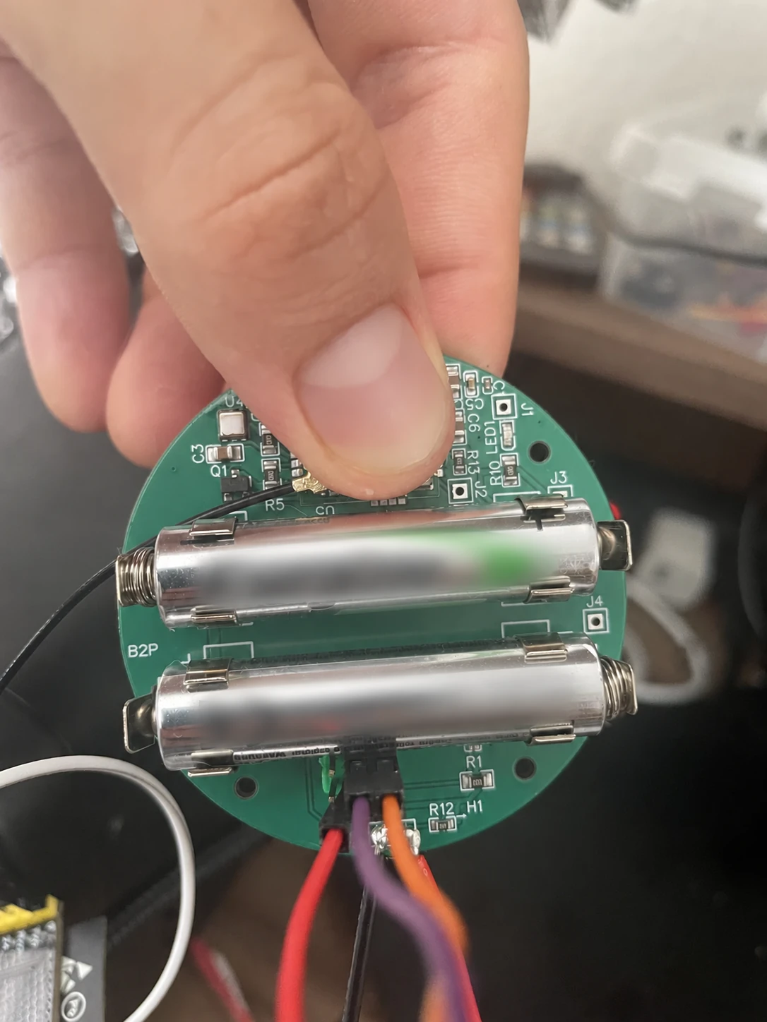 Circular green PCB held in a hand, with two batteries mounted across the board.